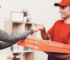 DoorDash delivery driver holding food orders near a busy restaurant.
