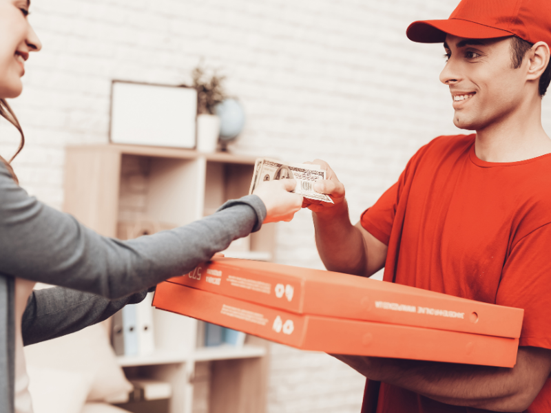 DoorDash delivery driver holding food orders near a busy restaurant.